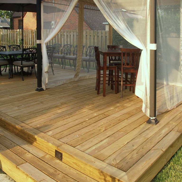 Tall wooden privacy fence with a mature tree incorporated into its structure and green lawn in the background.
